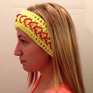 Peut inclure: Un bandeau crocheté jaune avec des coutures rouges, ressemblant à une balle de softball. Le bandeau est porté par une personne aux cheveux longs blonds.
