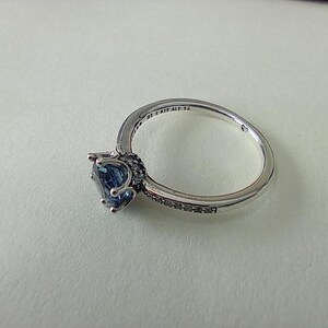 May include: A silver ring with a large, heart-shaped blue gemstone. The band is detailed with small, dark stones and the inscription "S 925 ALE 56". The ring is set against a white background.