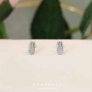 Puede incluir: Un par de pendientes de piña de plata con piedras de circonita cúbica transparentes. Los pendientes son pequeños y delicados, perfectos para el uso diario.