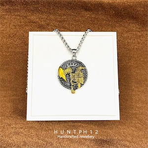 May include: A silver-toned necklace with a circular pendant featuring a gold-colored eagle and axe design. The pendant has a black and silver border with engraved text. The necklace is displayed on a white surface with the text "HUNT PH 12 Handcrafted Jewellery" at the bottom.