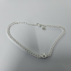 May include: A delicate silver anklet featuring a series of small, clear, round stones. The anklet includes a paw print charm with clear stones and a lobster clasp closure. The anklet is approximately 9 inches in length.