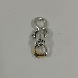 Puede incluir: Un charm de mono plateado con un anillo dorado. El mono está colgado boca abajo, con los brazos y las piernas alrededor del anillo. El charm tiene ojos negros y una expresión sonriente.
