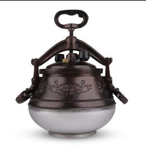 Op de afbeelding: Een vintage snelkookpan met een donkerbruin bovenstuk en een zilverkleurig onderstuk. Het heeft een handvat, een overdrukventiel en decoratieve bloempatronen. De pan is ontworpen voor gebruik op een fornuis.