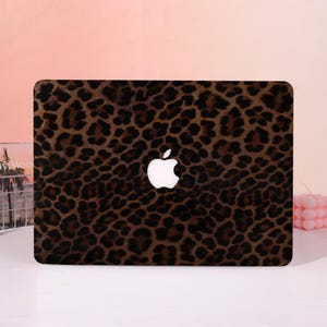 May include: A rectangular laptop cover featuring a brown and black leopard print pattern. The cover has a centred cutout displaying the white Apple logo. The design covers the entire surface of the laptop lid with a repeating animal skin motif.