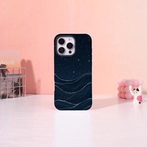 May include: A dark blue phone case featuring a starry night sky design with shimmering wave patterns. The case has a black border and a camera cutout. The design evokes a sense of the ocean under a starlit sky.