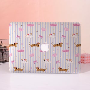 Può includere: Custodia per laptop con un motivo ripetuto di bassotti, fiocchi e cuori su uno sfondo a righe azzurre e crema. La custodia ha il logo Apple al centro e il testo "my little cute loves puppy".