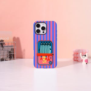 May include: A smartphone case featuring vertical blue and pink stripes. The center displays a graphic of a sardine tin with four blue fish, a red band, and yellow text reading SAR, along with smaller text including NET WT and Olive Oil.