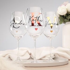 Op de afbeelding: Drie heldere wijnglazen met gepersonaliseerde namen en initialen. De glazen hebben een hartvormig ontwerp aan de basis. De namen "Sandra", "Kathi" en "Vivien" staan in een scriptletter op de glazen. De initialen zijn vetgedrukt.
