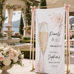 Puede incluir: Una pancarta vertical blanca con una ilustración de una copa de champán adornada con un collar de perlas, un ramo de flores rosa suave y texto negro que dice Pearls & Prosecco, Welcome to Sophia's Bridal Shower y 10.20.2026.