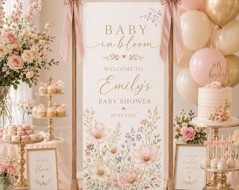 May include: A vertical rectangular welcome sign for a baby shower featuring the text Baby in bloom, Welcome to Emily's Baby Shower, and the date 09.09.2026. The sign is decorated with watercolor floral illustrations and held by a wooden frame with pink bows.