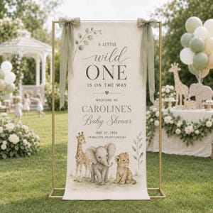 May include: A vertical rectangular banner on a gold metal frame featuring the text A LITTLE wild ONE IS ON THE WAY, WELCOME TO CAROLINE'S Baby Shower, MAY 17, 2026, CHARLESTON, SOUTH CAROLINA, with illustrations of a giraffe, elephant, and lion cub.