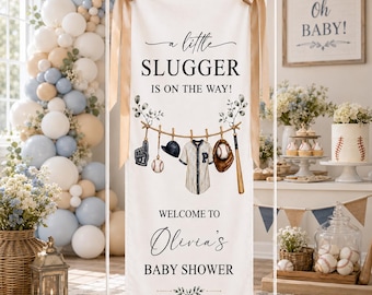 Peut inclure: Une bannière verticale blanche avec le texte A little SLUGGER IS ON THE WAY! et WELCOME TO Olivia's BABY SHOWER AUGUST 20, 2026. Le design présente des illustrations d'un gant de baseball, d'une batte, d'une balle, d'une casquette et d'un maillot.