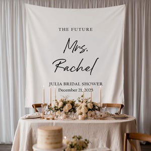 Puede incluir: Una mesa decorada para una despedida de soltera, con un mantel blanco, arreglos florales, velas y cubiertos. Una pancarta en el fondo muestra el texto "The Future Mrs. Rachel" y la fecha.