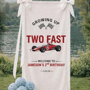 May include: White banner with the text "Growing Up Two Fast" and a red race car graphic. The banner reads "Welcome to Jameson's 2nd Birthday" with the date 3.22.24. White bows adorn the top corners.