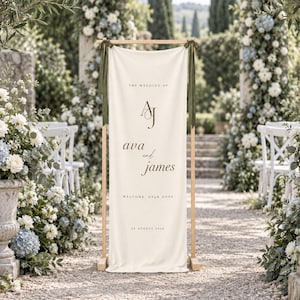 May include: A vertical cream-colored fabric wedding welcome sign suspended from a light wood frame with dark green ribbons. The sign features the text: THE WEDDING OF, AJ, ava and james, WELCOME, DEAR ONES, and the date 24 AUGUST 2024 in dark brown.