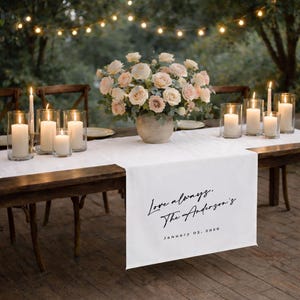 May include: A wooden table set for a special occasion, adorned with a white table runner, candles, and a floral centerpiece. The table runner has the text "Love always. The Anderson's. January 03, 2026."