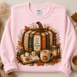 Peut inclure: Un sweat-shirt à col rond rose clair avec un motif de citrouille composée de livres empilés, portant le texte Just One More Chapter et un cœur. Le design inclut un livre ouvert, des lunettes rondes, une tasse avec une citrouille et une lanterne.