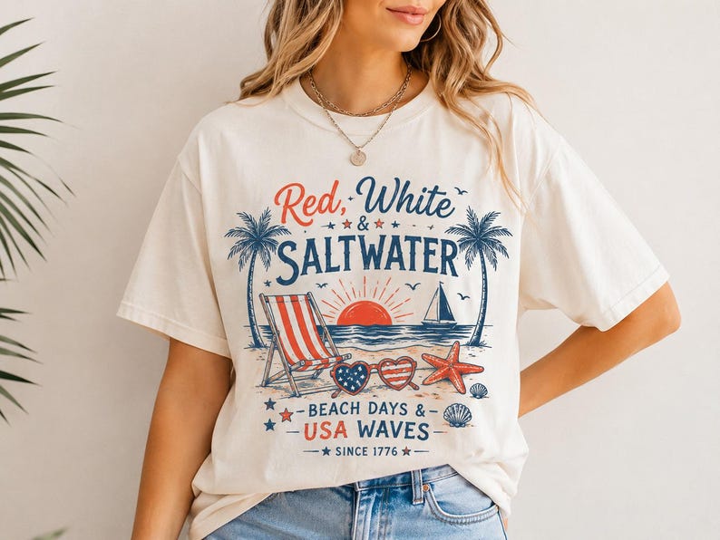 May include: A cream-colored short-sleeve t-shirt featuring a graphic print with the text Red, White & SALTWATER, BEACH DAYS & USA WAVES, and SINCE 1776. The design includes palm trees, a beach chair, a sailboat, heart-shaped sunglasses, and a starfish.