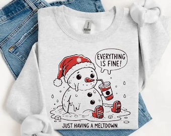 Può includere: Felpa a maniche lunghe grigio cenere con grafica di un pupazzo di neve che si scioglie, con cappello rosso e che beve da un bicchiere. Il testo recita: "EVERYTHING IS FINE!" e "JUST HAVING A MELTDOWN."