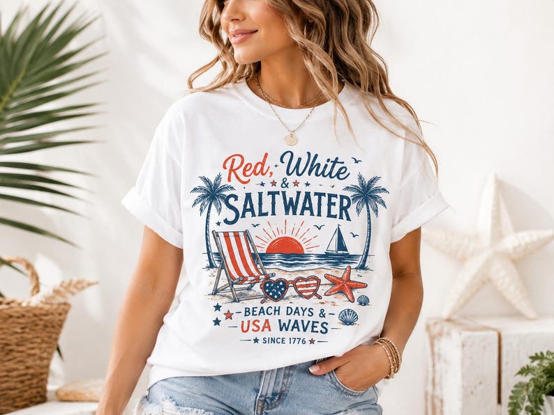 May include: A white t-shirt featuring a graphic print with the text Red, White & SALTWATER and BEACH DAYS & USA WAVES SINCE 1776. The design includes palm trees, a beach chair, a sailboat, a sun, heart-shaped sunglasses, a starfish, and seashells.