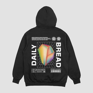 Könnte beinhalten: Schwarzer Kapuzenpullover mit großem Grafikdruck auf dem Rücken. Die Grafik zeigt eine geometrische, mehrfarbige Form über einem Raster mit den weißen Worten "DAILY BREAD". Zusätzlicher Text und ein Barcode sind ebenfalls vorhanden.