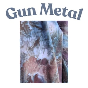 May include: A piece of fabric featuring a tie-dye pattern with blended shades of brown, blue, and white. The text "Gun Metal" is printed in a grey, curved font above the fabric, which displays a marbled, organic appearance with soft color transitions.