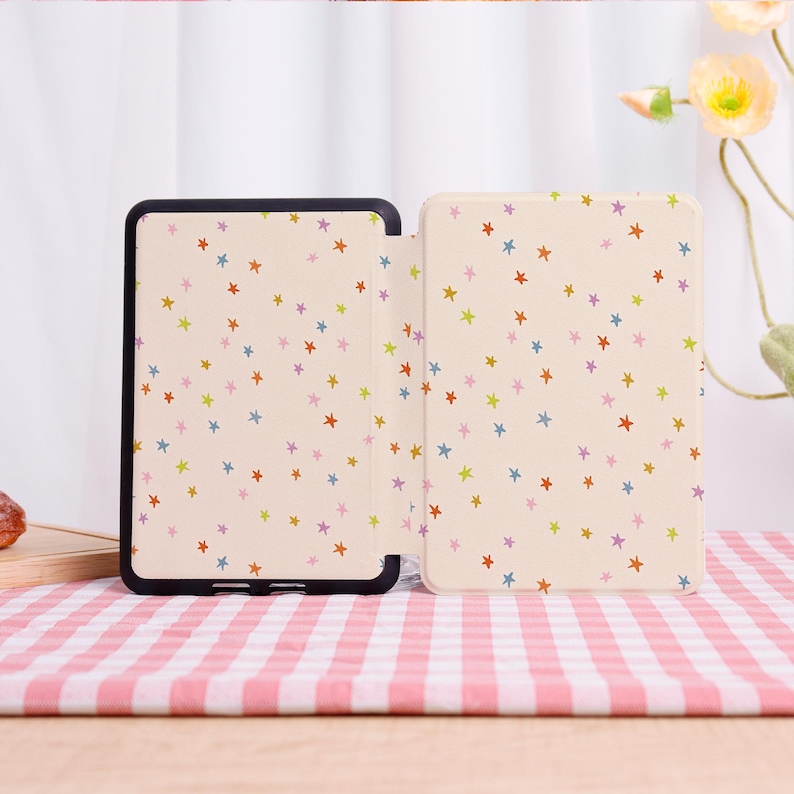 Pode incluir: Uma capa de tablet bege com uma borda preta, aberta para revelar um interior estampado. A capa e o interior apresentam um padr&atilde;o repetitivo de estrelas coloridas em tons de vermelho, azul, verde e roxo. A capa est&aacute; sobre uma superf&iacute;cie xadrez rosa e branca.