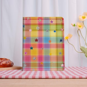 May include: A colorful plaid notebook with a variety of star-shaped stickers. The notebook features a vibrant pattern of pink, yellow, green, and blue squares. The stars are in various colors, including silver, red, and gold.