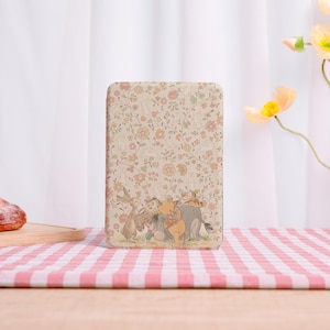 May include: A rectangular, beige case featuring a floral pattern with cartoon characters. The design includes Winnie the Pooh, Piglet, Tigger, and Rabbit. The case is set on a red and white checkered tablecloth.