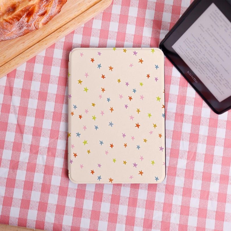 Pode incluir: Uma capa Kindle creme adornada com um padr&atilde;o de estrelas coloridas. A capa &eacute; retangular e serve para um dispositivo Kindle. O fundo &eacute; um padr&atilde;o xadrez rosa e branco.