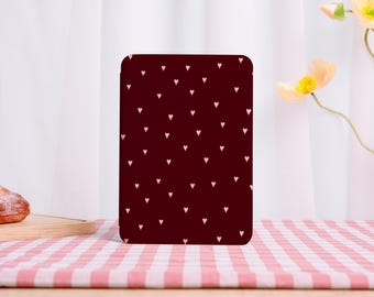 May include: A rectangular tablet or e-reader case featuring a deep burgundy background adorned with a repeating pattern of small, light pink hearts distributed evenly across the entire surface of the front cover.