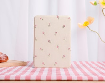 May include: A rectangular e-reader case featuring a cream-colored background with a repeating pattern of small pink flowers and green stems. The case has a smooth, matte finish and is positioned upright on a surface with a pink and white checkered pattern.