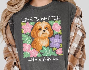 May include: Dark gray t-shirt with the text "Life is Better with a Shih Tzu." The shirt features a graphic of a Shih Tzu dog surrounded by pink, purple, and green floral elements. The shirt is a casual style.
