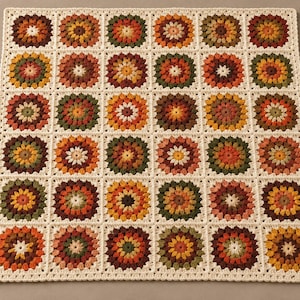 May include: A square crochet blanket featuring a grid of thirty-six individual floral motifs. Each motif is composed of concentric circles in shades of orange, yellow, brown, and green, all bordered by a cream-colored yarn frame.