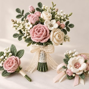 May include: A crochet floral set featuring a bouquet, a boutonniere, and a wrist corsage. The arrangement includes pink and cream roses, small white filler flowers, and green leaves. The bouquet handle is wrapped in cream lace with a matching bow.
