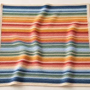 May include: A square crochet blanket featuring horizontal stripes in shades of blue, green, yellow, orange, and red. The blanket is finished with a solid cream-colored border that frames the multicolored striped pattern throughout.