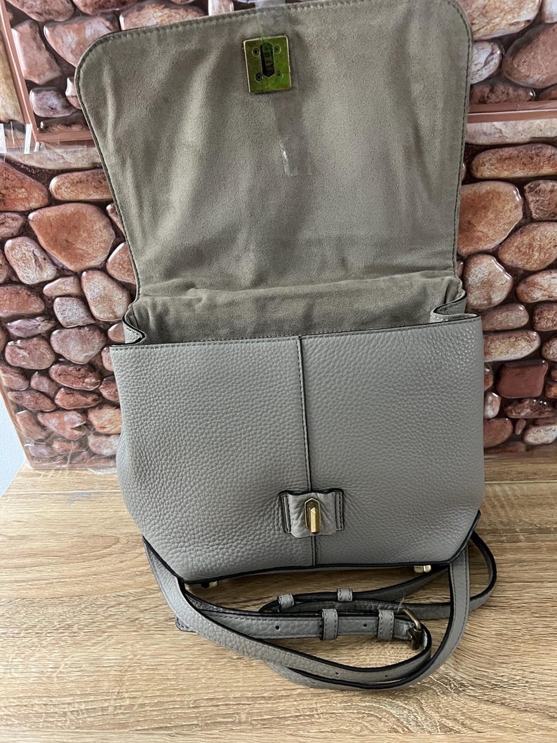 Pu&ograve; includere: Borsa a tracolla in pelle grigia con chiusura a patta e tracolla regolabile. La borsa presenta una finitura strutturata e una chiusura color oro. L'interno &egrave; foderato con un tessuto grigio pi&ugrave; chiaro. La borsa &egrave; aperta.