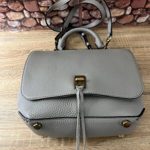 Pu&ograve; includere: Una borsa a mano in pelle grigia con manico superiore e tracolla. La borsa ha una chiusura a patta con una chiusura color oro e borchie decorative. La borsa ha una superficie strutturata e un piccolo dettaglio a nappa.