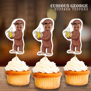Puede incluir: Tres cupcakes con glaseado blanco, cada uno coronado con un adorno para cupcakes de Curious George. Los adornos presentan una imagen de dibujos animados de Curious George sosteniendo un plátano. El texto "CURIOUS GEORGE CUPCAKE TOPPERS" está en la parte superior.