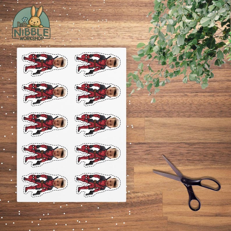 May include: A sheet of stickers featuring a Deadpool-themed design. Each sticker shows a figure in a red and black costume with a light skin tone. The stickers are on a white background. A pair of scissors is next to the sheet.
