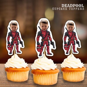 May include: Three cupcakes with white frosting, each topped with a Deadpool-themed image. The Deadpool images feature a child's face superimposed on the character's costume. The cupcakes sit on a wooden surface. Text at the top reads "DEADPOOL CUPCAKE TOPPERS."