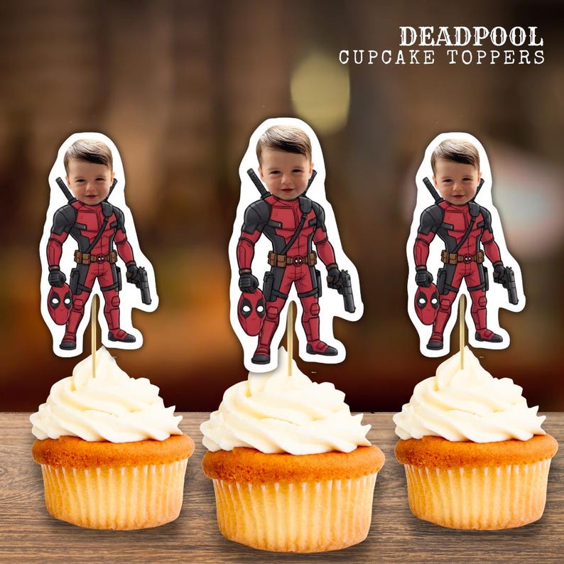 May include: Three cupcakes with white frosting, each topped with a Deadpool-themed image. The Deadpool images feature a child's face superimposed on the character's costume. The cupcakes sit on a wooden surface. Text at the top reads "DEADPOOL CUPCAKE TOPPERS."