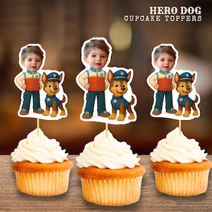 Puede incluir: Tres cupcakes cubiertos con adornos para cupcakes de Hero Dog. Cada adorno presenta a un niño y un perro de dibujos animados. El niño viste un atuendo azul, naranja y blanco. El perro es un perro policía marrón y canela. Los cupcakes tienen bizcocho amarillo y glaseado blanco.