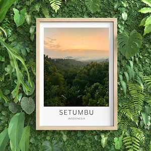 Peut inclure: Une affiche encadrée représentant un paysage forestier verdoyant sous un ciel de lever ou coucher de soleil. Le texte "SETUMBU" et "INODONESIA" est imprimé en blanc en bas. Le cadre est en bois clair.