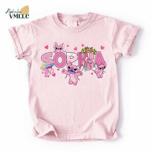 A pink t-shirt with a design featuring the characters from the Disney movie "Stitch". The characters include a pink bunny, a pink cat, and a pink dog, along with the name "Sophia" written in pink letters.