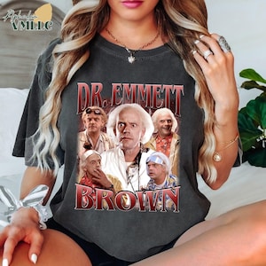 May include: Dark gray t-shirt featuring a graphic of Dr. Emmett Brown from the movie Back to the Future. The graphic includes the text "DR. EMMETT BROWN" in a red and white font, along with multiple images of the character.