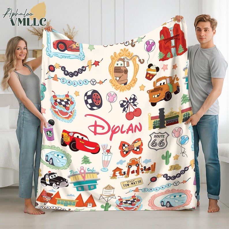 A man and a woman are holding up a large blanket with various cartoon car designs and other car-related items, such as a fire hydrant, traffic light, and gas station.