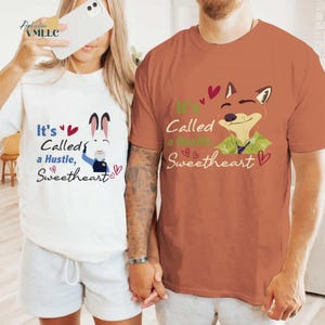 A man and a woman are standing together, both wearing t-shirts with a cartoon fox and text. The man is wearing a brown t-shirt, and the woman is wearing a white t-shirt.