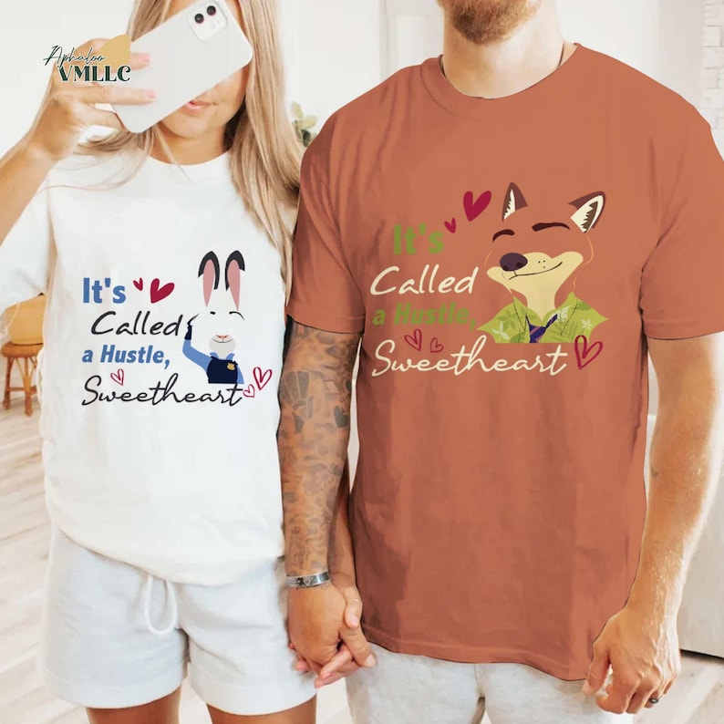 A man and a woman are standing together, both wearing t-shirts with a cartoon fox and text. The man is wearing a brown t-shirt, and the woman is wearing a white t-shirt.