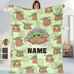 May include: A light green fleece blanket featuring a repeating pattern of the character Grogu in various poses, including one large central illustration of Grogu inside a floating pod. The word NAME is printed in large, dark brown block letters.